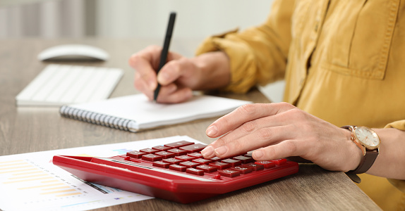 Professional accountant using calculator at wooden desk in office, closeup