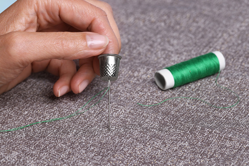 Woman sewing on grey fabric with thimble and needle, closeup
