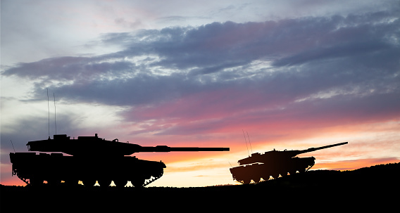 Silhouettes of army tanks at sunset sky background. Military machinery.