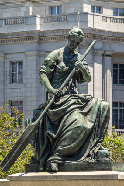 San Francisco, CA, USA - July 12, 2023: Pioneer monument on Fulton street, woman with oar impersonating commerce statue on south side. White public library facade as backdrop. Some green foliage