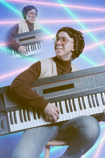 A late 1980's - early 1990's emulation of a bad school portrait, complete with tacky pink and cyan lasers in the blue background of a young nerd in a turtleneck with a sweater vest and gold chain.  He holds onto a vintage looking keyboard synthesizer.  Low contrast and bad posing; glamour shots at their best/worst!