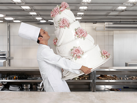 Male chef carrying wedding cake in a commercial kitchen