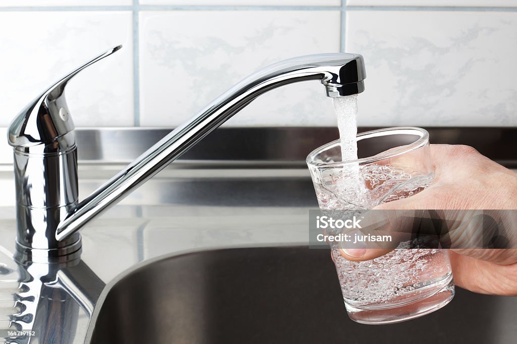 Glass filled with drinking water from kitchen faucet. Hand holding a glass of water poured from the kitchen faucet. Faucet Stock Photo