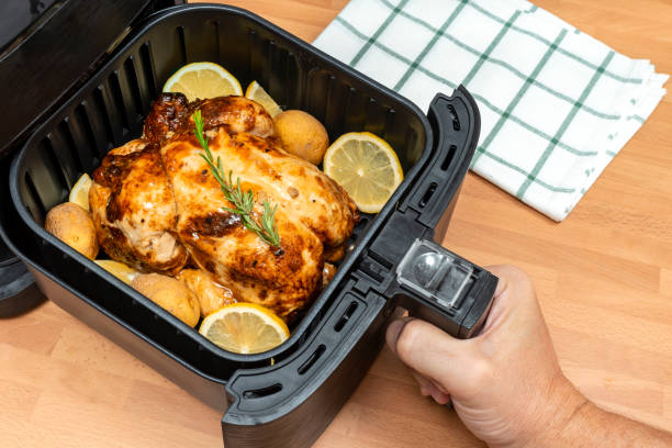 HAND COOKING WHOLE ROASTED CHICKEN WITH GARNISH IN AIR FRYER AT THE KITCHEN. TOP VIEW. HAND COOKING WHOLE ROASTED CHICKEN WITH GARNISH IN AIR FRYER AT THE KITCHEN. TOP VIEW. deep fryer stock pictures, royalty-free photos & images