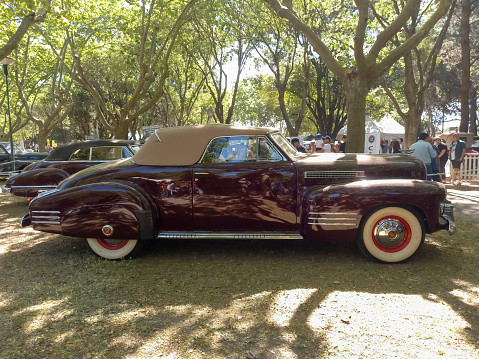 San Isidro, Argentina - Oct 7, 2022: Old red burgundy 1941 Cadillac Series 62 coupe convertible V8 in a park. Nature, grass, trees. Sunny day. Autoclasica 2022 classic car show.