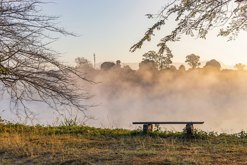 Bench in a park on a sunny autumn morning with foggy