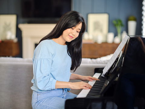 An adult Korean Asian woman, practicing piano in a home.