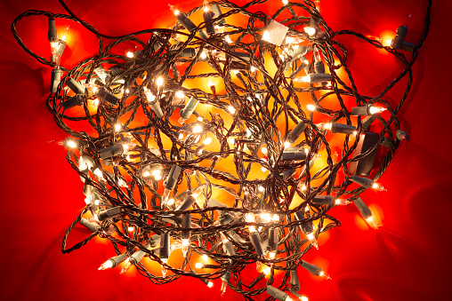 Christmas lights turned on with the cord all tangled up on red colored background