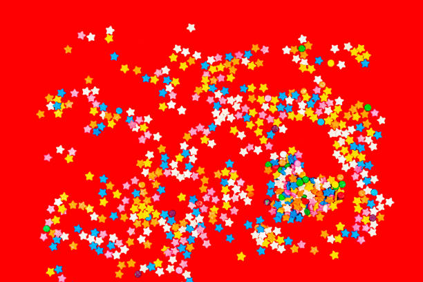 High angle view of sugar sprinkles of star shape over red color background and also a group of sugar sprinkles in heart shape form . Image made in studio.