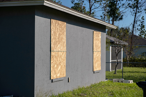 Plywood mounted as storm shutters for hurricane protection of house windows. Protective measures before natural disaster in Florida.