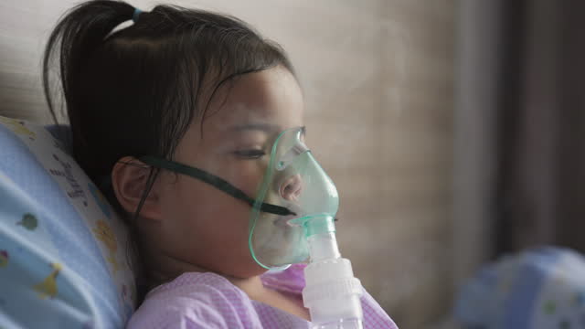A courageous Asian little girl takes a moment to breathe through an inhaler mask