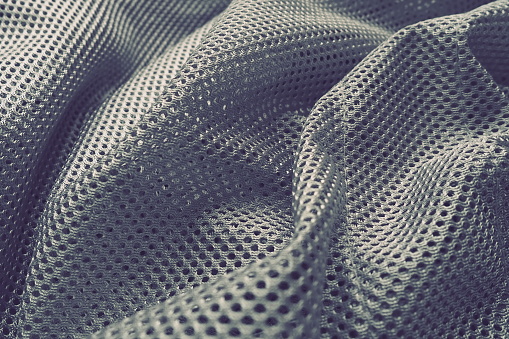 Synthetic fabric with holes laid in waves. Beautiful drape. Fabric for curtains, interior design, and decor. Wrinkled gray fabric