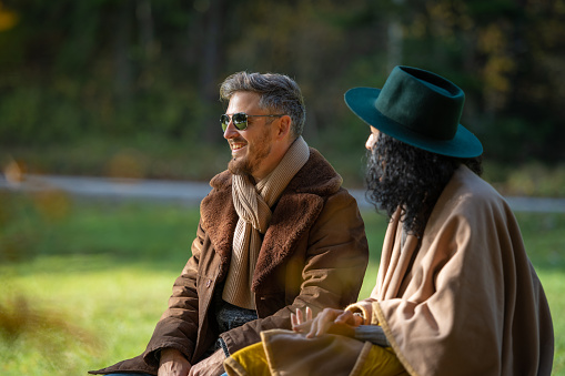 A young Latino woman and a white man are having a friendly conversation. A man with sunglasses, a woman with a green hat and a poncho. Autumn.