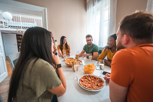 Multi-racial friends sitting at a table in a domestic living room. Gathering for a friends birthday party.