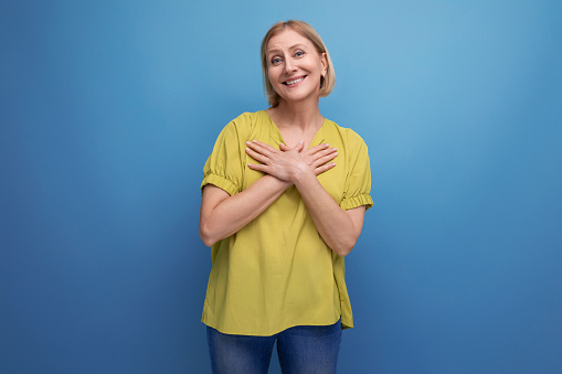 attractive 50s blonde woman in yellow t-shirt on blue background.