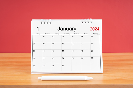 January 2024, Monthly desk calendar for 2024 year on wooden table with red color background.