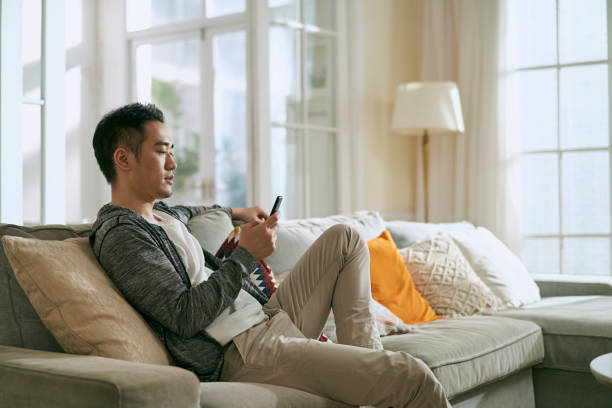 young asian man using mobile phone at home stock photo