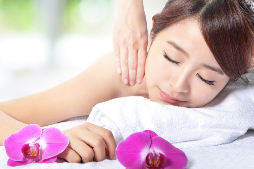 Close up of a young beautiful woman getting spa massage on shoulder with orchid. asian beauty