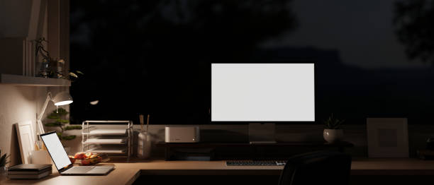 istock Modern office workspace at night with a computer and laptop on a table with office supplies. 1647550465