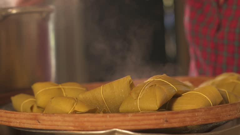 Woman's hands removing the cooked Pamonhas from the pan and placing them in the sieves. Typical Brazilian food with green corn. Collection of themed videos.