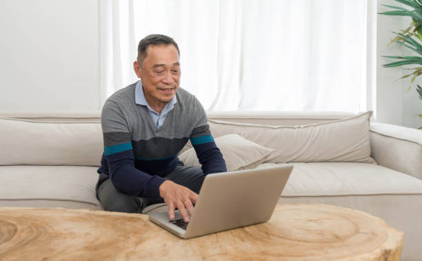 istock Home office scenario capturing senior man comfortably sitting on a couch, busy working or surfing the internet on his laptop. 1647653899