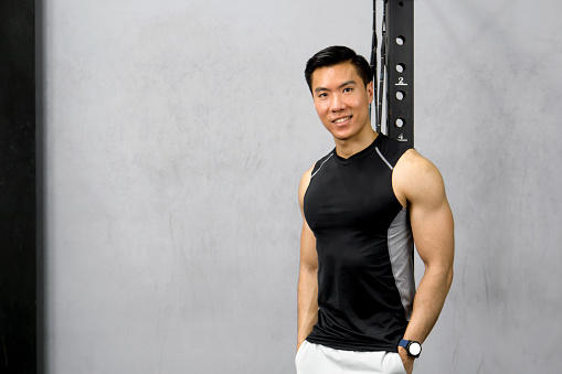 Athletic male in black tank top and white shorts posed before a fitness center backdrop.