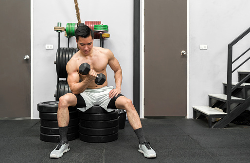 A muscular man energetically performs a strength-training exercise in a well-equipped gym. He is intensely focused while lifting heavy dumbbells.