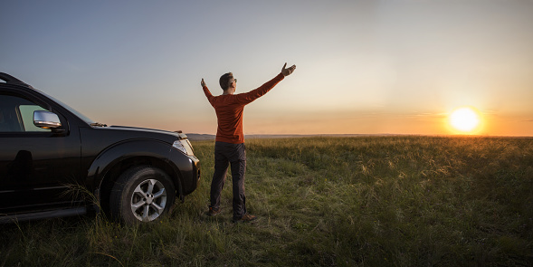 freedom. man stands near his car at nature and watching the sunset or sunrise. banner with place for text.