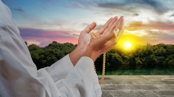 Muslim man praying with prayer beads in his hands with the sunset scene background
