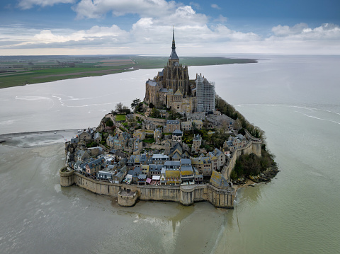 Mont Saint-Michel on tidal Island under sunny summer skyscape. Aerial Drone Point of view from the Atlantic Ocean Side over Mont Saint Michel towards the Normandy Coast. Mont Saint-Michel, Avranches, Manche, Normandy, France, Europe