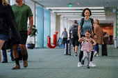 Excited toddler girl running through the airport with her mom