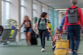Toddler girl riding on suitcase through an airport while traveling with her mom