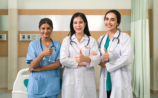 A snapshot of affirmation and medical success, featuring three female healthcare professionals giving thumbs up within a modern hospital room setting.