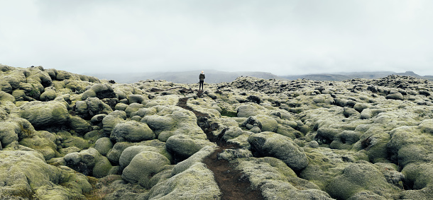 Woman standing at the end of the path leading through the mossy lava field in Iceland.