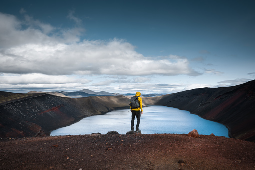 Man standing on top of colorful Ljotipollur crater lake in the south highlands of Iceland.
