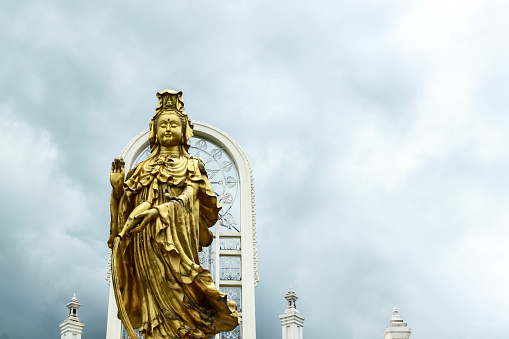 Golden Guanyin statue that is being built on a tall building for Thai and Chinese people People all over the world worship with backgrounds. White and gray clouds that look warm during the rainy seaso