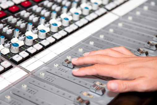 A handing adjusting the levels on an audio mixing board.