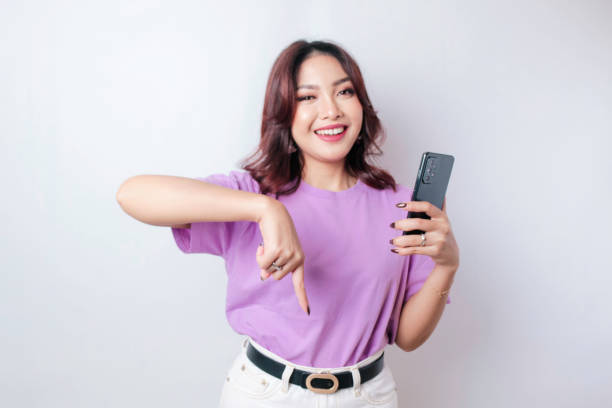 istock Smiling beautiful Asian woman pointing finger down to empty space isolated white background 1647882005