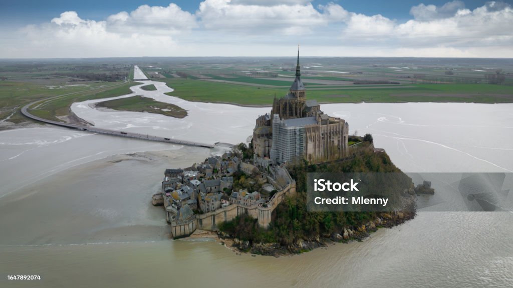 Normandy France Mont Saint-Michel Abbey Aerial Panorama Mont Saint-Michel on tidal Island under sunny summer skyscape. Aerial Drone Point of view from the Atlantic Ocean Side over Mont Saint Michel towards the Normandy Coast. Mont Saint-Michel, Avranches, Manche, Normandy, France, Europe Abbey - Monastery Stock Photo