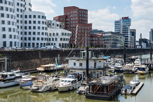 Dusseldorf, Germany - June 2, 2022: Street view of Dusseldorf at day with Media Harbour, boats in the foreground and contemporary architecture (Neuer Zollhof) in North Rhine-Westphalia, Germany.
