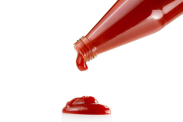 Ketchup dripping from a bottle to a white surface stock photo