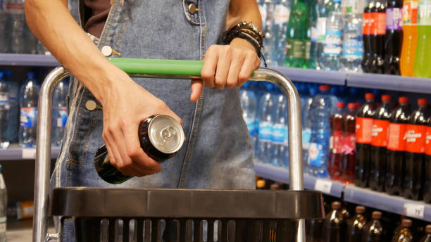 Close-up of a young woman's hands putting a can of soda or enerdy drink into a shopping cart stock photo