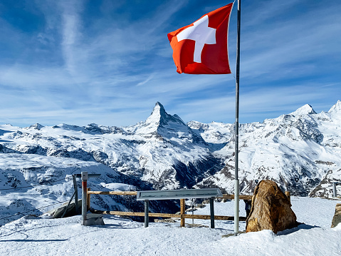 World famous mountain peak Matterhorn above Zermatt town in Mattertal, Valais canton, Switzerland, in winter with Switzerland national flag.