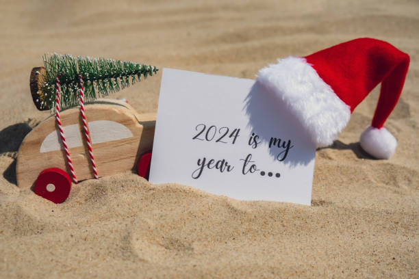 2024 IS MY YEAR TO... text on paper greeting card on background sandy beach sun coast. Christmas balls Santa hat New Year New Me Resolutions decoration. Summer vacation decor. Holiday concept calendar date postcard. Getting away Travel Business concept 2024 es mi aÑo para.. texto sobre papel tarjeta de felicitación en el fondo playa de arena sun coast. bolas de navidad sombrero de papá noel año nuevo nuevo me resoluciones decoración. decoración de vacaciones de verano. concepto de vacaciones calend