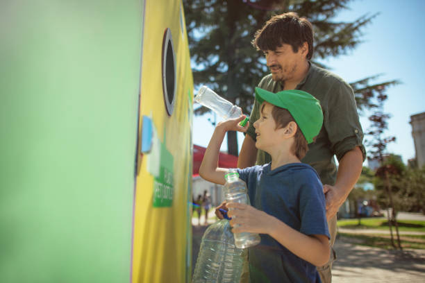 Father teaching his little boy to recycle plastic waste using correct garbage bin at a city street