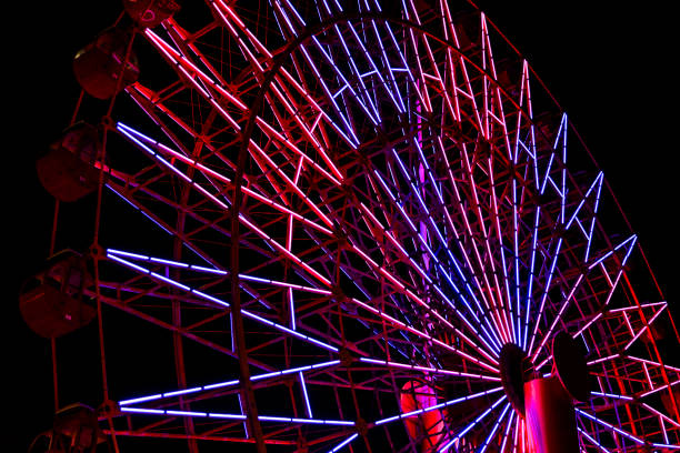 Red and purple light fluorescent on structure of ferris wheel with dark night background.