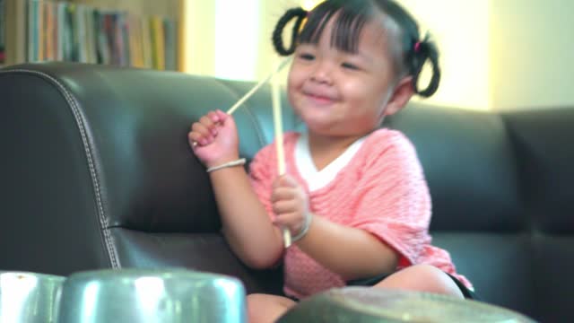Asian little girl playing pots and pans up sofa at home .