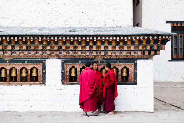 부탄 푸나카의 치미 라캉 수도원(chimi lhakang monastery)에서 종교 기도 바퀴 옆에 서 있는 세 명의 불교 학생 승려들 - bhutan himalayas buddhism monastery 뉴스 사진 이미지