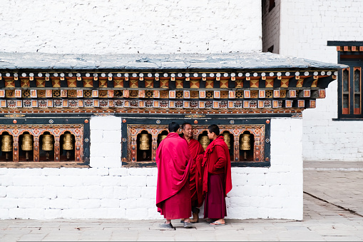 Punakha, Bhutan - 03 Desember, 2018: three Buddhism student monks standing by the religious prayer wheels at Chimi Lhakang Monastery, Punakha, Bhutan. High quality photo