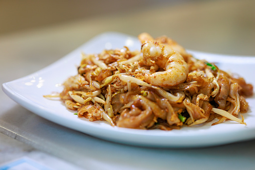 Penang famous street food, wok-fried rice noodles with scallop, egg, bean sprouts, prawns, chives, soy sauce and chili paste.